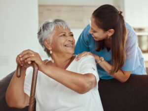 woman with a walking cane happily sitting with a nurse